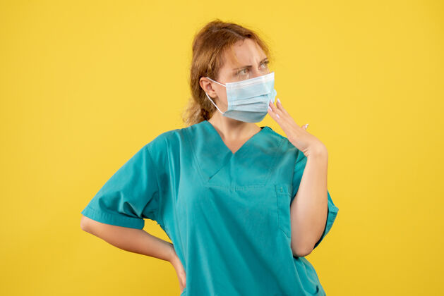人身着医疗服 戴着口罩的年轻女医生在黄墙上思考的正面图医学套装面具