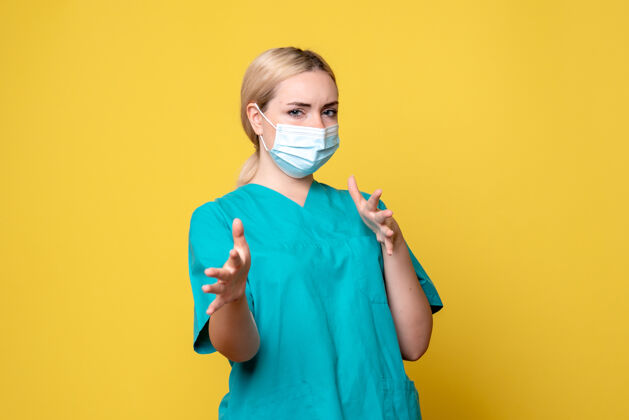 面具黄墙上年轻女医生穿着医用衬衫 戴着口罩的正面图快乐情绪人