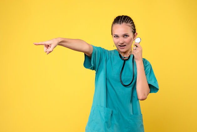 医生黄色墙壁上穿着带听诊器的医疗服的女医生的正视图人套装医学