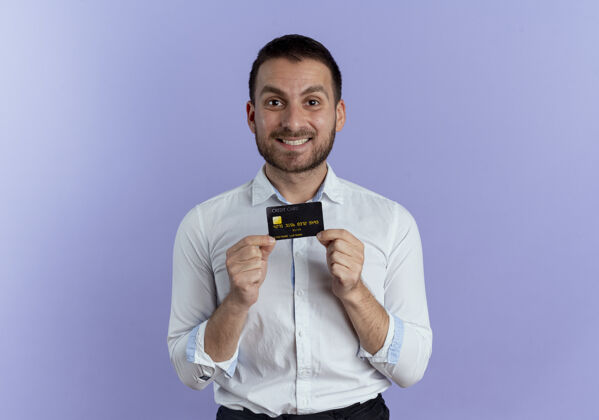 年轻笑容可掬的帅哥拿着信用卡孤零零地站在紫色的墙上成人商人男人
