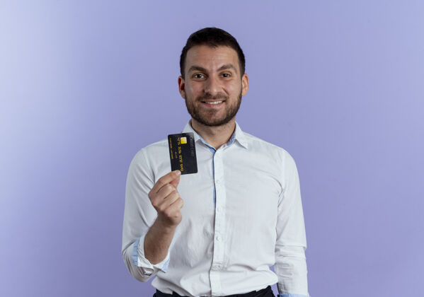 微笑笑容可掬的帅哥拿着信用卡孤零零地站在紫色的墙上持有紫色信用