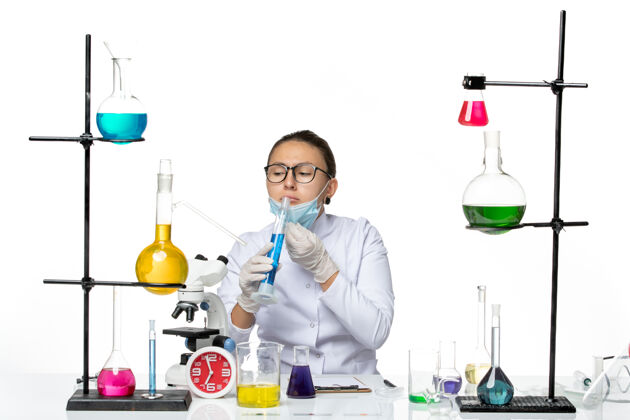 视图前视图穿着医疗服的女化学家戴着面具拿着白色背景上蓝色溶液的烧瓶飞溅着病毒化学实验室的病毒飞溅药物实验室