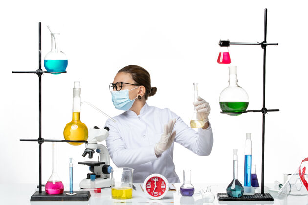 持有前视图：身穿白色医疗服的女化学家 带面罩 背景为浅白色 化学家实验室病毒冠状病毒飞溅医疗病毒实验
