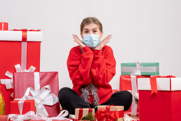 地板正面图：年轻女性戴着无菌面具坐着 手里拿着圣诞礼物面具礼物健康
