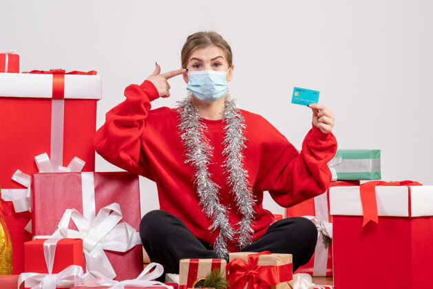 绝育正面图：年轻女性戴着无菌面具坐着 手里拿着圣诞礼物礼物病毒人