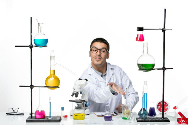 医学前视图身穿白色医疗服的男性化学家坐在白色背景病毒实验室共患疾病科学的解决方案液体科学容器