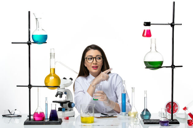 容器正面图：身着白色医疗服的女化学家拿着装有溶液的烧瓶 放在白色办公桌上 是科学病毒冠状病毒大流行实验室实验室溶液罐子