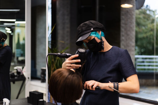 脸一个专业的女理发师给客户理发这个女孩戴着面具坐在美容院里设备人肖像