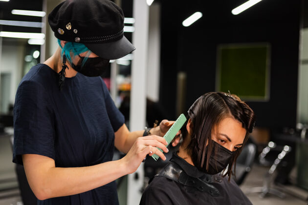 设备一个专业的女理发师给客户理发这个女孩戴着面具坐在美容院里流行理发师客户