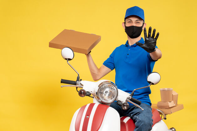 男人正面图身穿蓝色制服的男信使拿着食品盒 骑着黄色病毒大流行的柯维德送货工作自行车黄色男信使送货