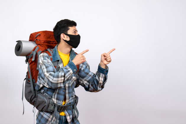 视图正面图：有兴趣的男性旅行者背着背包和面具指着什么东西活跃快乐面具