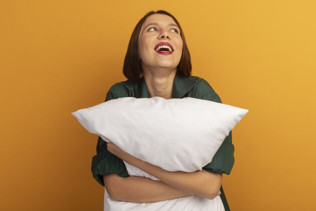 姿势快乐美丽的白种女人抱着枕头 看着橙色的边漂亮黑发壁板
