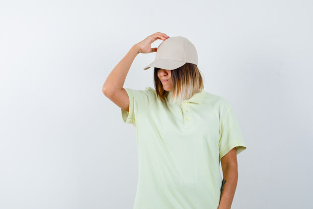 微笑年轻女性穿着t恤 戴着帽子 手举着头 看上去很体贴 前视图持有模型时尚