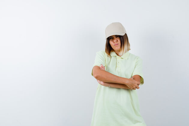年轻年轻女性交叉双臂站在t恤衫上 戴着帽子 看起来很自信前视图前面水疗美容
