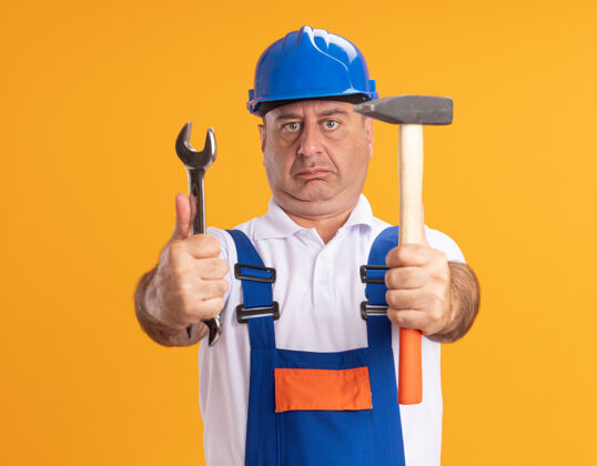 锤子印象深刻的白人成年建筑工人在制服举行扳手和锤子对橙色人人建筑工人