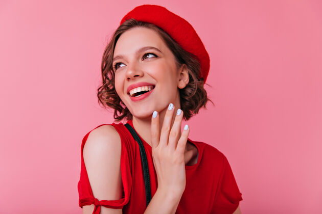 配件幸福的法国女人 带着白色的指甲笑着室内拍摄的快乐卷曲的女孩 戴着红色贝雷帽 微笑着看着别处成人寒冷贝雷帽