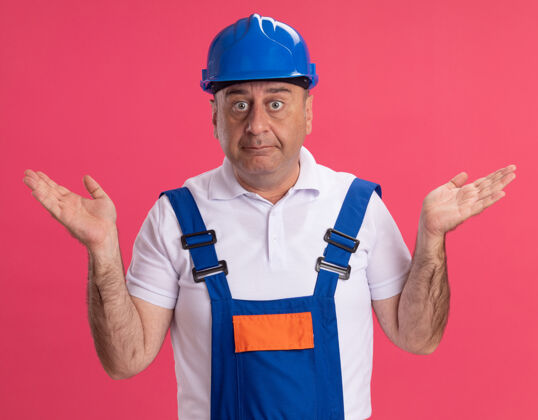 困惑困惑的成年白人建筑工人穿着制服 双手张开放在粉红色的地板上手男人建设者