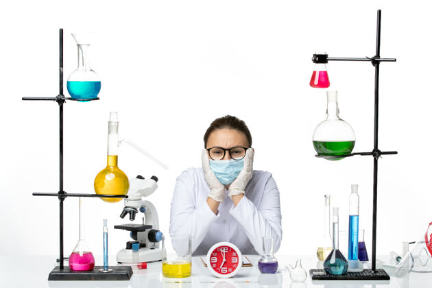 西装前视图：穿着医疗服的女化学家 戴着面罩 坐在白色背景上的解决方案病毒实验室化学covid飞溅实验室坐前面