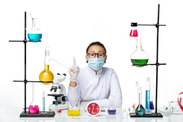 医生前视图穿着白色医疗服的女化学家带着面罩坐在浅白背景上的溶液化学家实验室病毒-飞溅医学病毒实验室