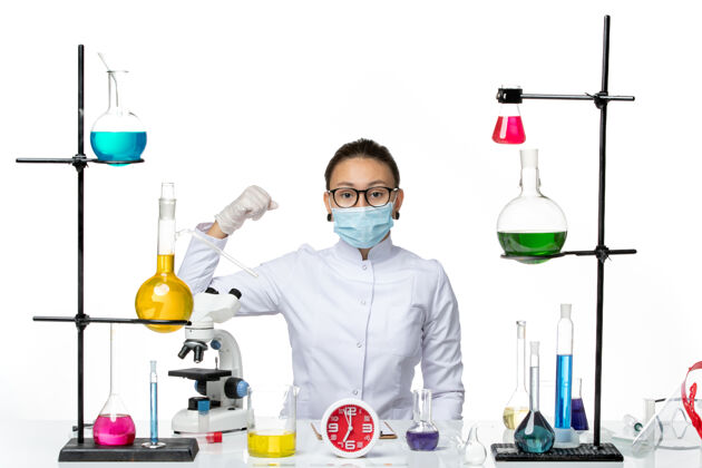 实验室前视图穿着医疗服的女化学家戴着面罩 坐在浅白背景上的解决方案病毒实验室化学冠状病毒飞溅视图医生套装