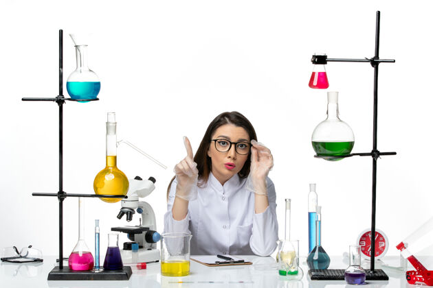 容器前视图穿着医疗服的女化学家围坐在桌子旁 拿着白色背景的解决方案实验室病毒冠状病毒-大流行科学套装桌子酒