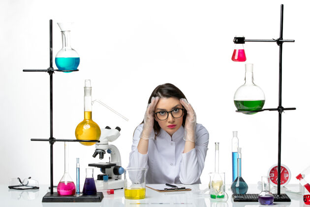 坐着前视图穿着医疗服的女化学家围坐在桌子旁 在浅白色背景上提供解决方案实验室病毒冠状病毒大流行科学化学溶液视图