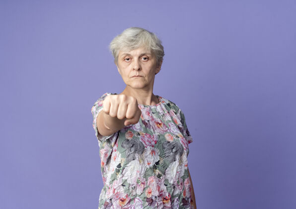 自信自信的老妇人孤零零地在紫色的墙上伸出拳头坚持老老人