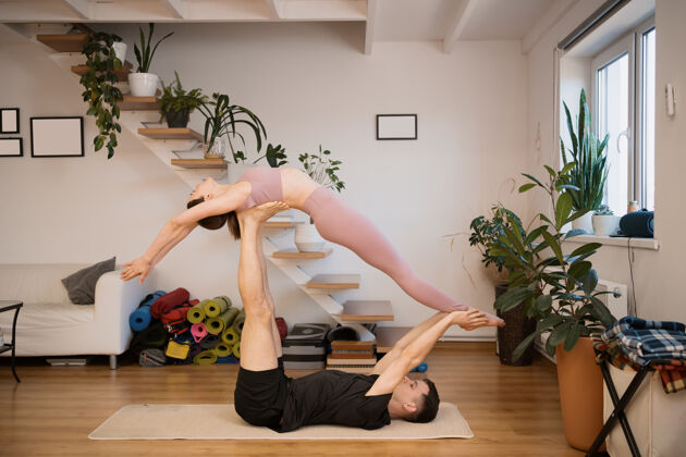生活一对年轻的情侣在家里一起练习acro瑜伽在现代室内爱好 团结 健康的生活方式运动服锻炼夫妻