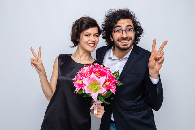 三月年轻漂亮的夫妇幸福的男人和女人拿着花束看着镜头微笑着愉快地竖起大拇指庆祝三八国际妇女节站在白色的背景下节日花束情侣