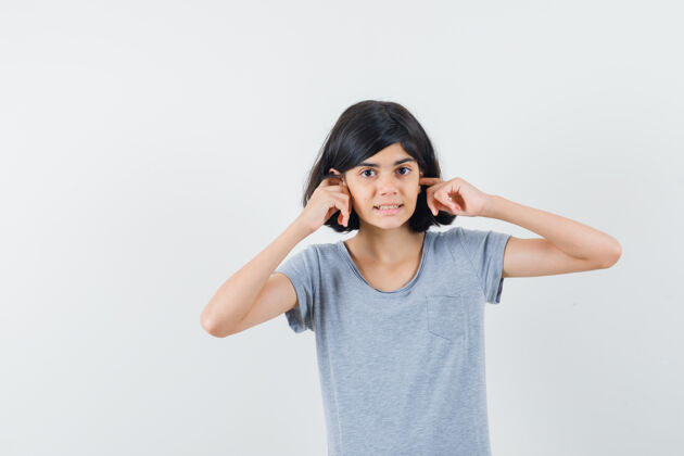 室内小女孩用手指塞住耳朵 穿着t恤衫 看上去很困惑 前视图耳朵动物童年