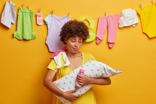 小新生儿睡在母亲的手上困惑的女人抱着裹着毛巾的婴儿 奶瓶里放着牛奶 照顾着婴儿 不明白女儿为什么哭 忙着做家务宝贝新生儿拥抱