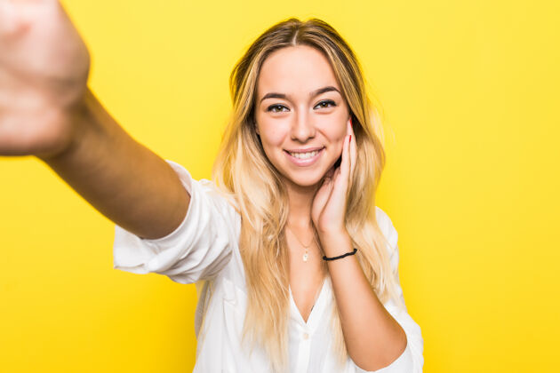 年轻一个微笑的年轻女子在黄色墙壁上自拍的肖像电话电话手机