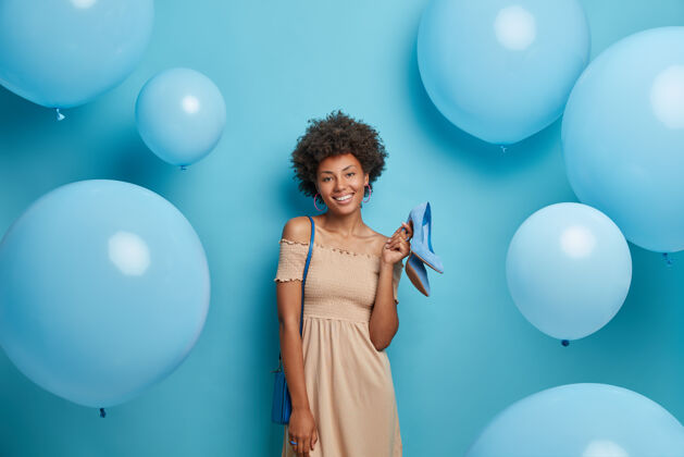 西装穿着时髦连衣裙的快乐优雅的女人 肩上扛着蓝色的包 手里拿着高跟鞋 对着节日的气球摆姿势 准备庆祝什么 为派对做准备女人和时尚概念请服装积极