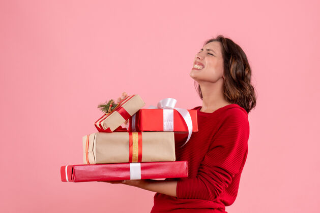 携带正面图年轻的女性拿着圣诞礼物站在粉红色的椅子上丝带节日美丽