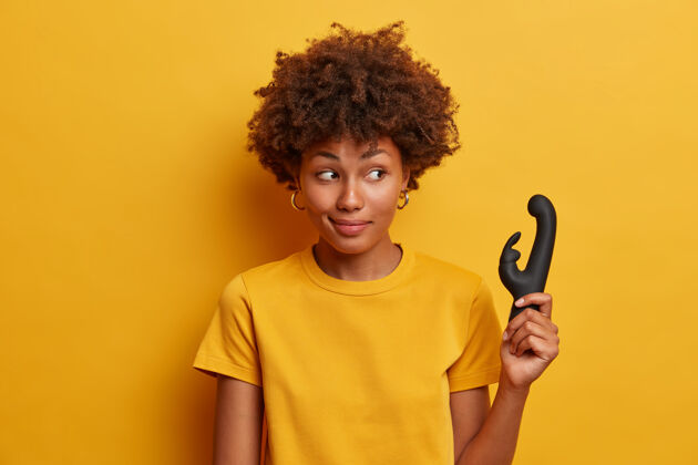 刺激黑皮肤女性的照片提供性技巧 建议购买用于提供阴蒂高潮和刺激的振动器 享受单独手淫 在黄色墙壁上获得孤立的乐趣内部按摩非洲