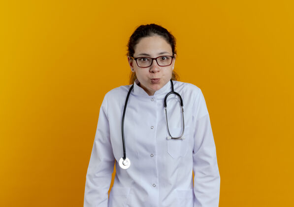 长袍高兴的年轻女医生穿着医疗袍和听诊器与眼镜隔离橙色年轻人医生