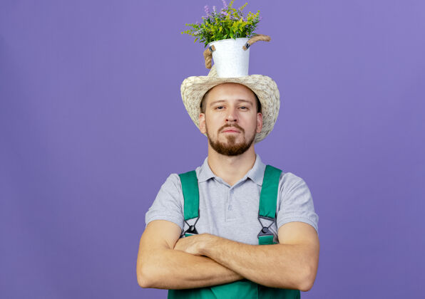帽子自信的年轻英俊的斯拉夫园丁 身着制服 戴着帽子 站在那里 头上抱着花盆 看上去与世隔绝花盆自信立场