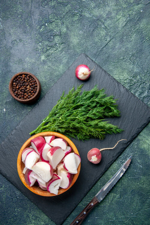 食物新鲜莳萝束和整个切碎的萝卜刀在黑色砧板上的俯视图胡椒刀在绿-黑混合色背景上的自由空间新鲜萝卜免费