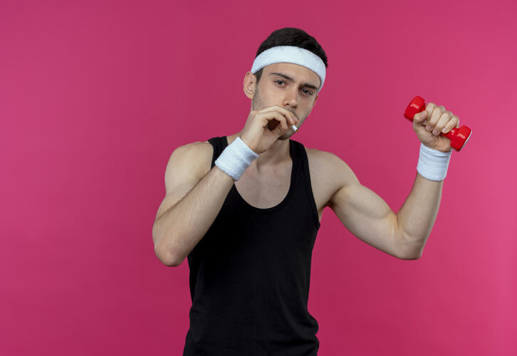 头带戴着头巾 手持哑铃 站在粉色背景下抽烟的年轻运动型男子工作吸烟运动
