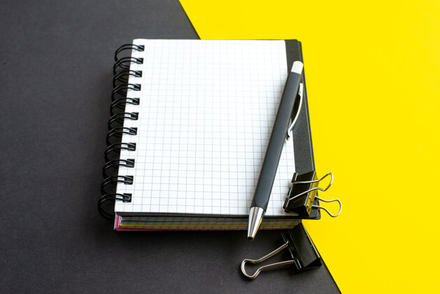 螺旋笔记本侧视图螺旋笔记本上的书和笔在黑黄色背景与自由空间活页夹钢笔办公室