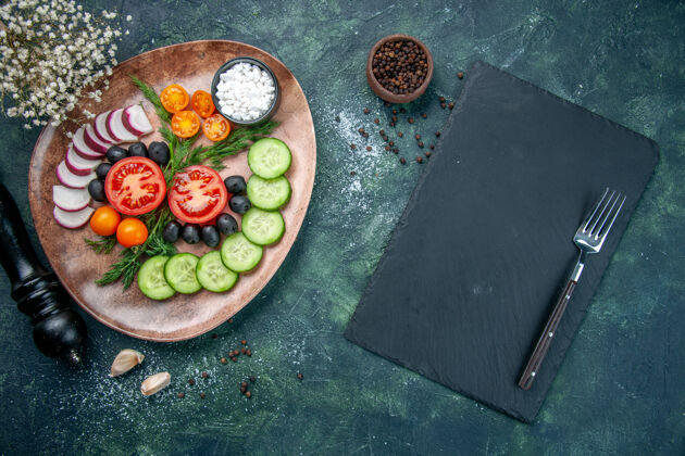 叉子顶视图新鲜切碎的蔬菜橄榄盐在一个棕色的盘子和厨房锤子大蒜素叉在绿色和黑色混合色背景的木制砧板盘子厨房盘子