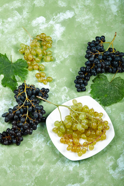 美味一盘白葡萄和黑葡萄 绿色背景上有叶子高质量的照片自然盘子正面视图