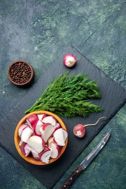食物新鲜莳萝束和整个切碎的萝卜刀在黑色砧板上的俯视图胡椒刀在绿-黑混合色背景上的自由空间新鲜萝卜免费