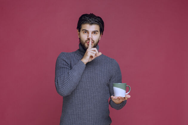 年轻一个穿着灰色毛衣的男人拿着一个咖啡杯 要求安静茶人成人