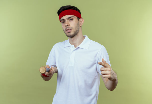 年轻戴着头巾的年轻运动型男子拿着棒球棒 手指指着塞梅拉 站在绿色背景上 看上去很自信自信头带手指