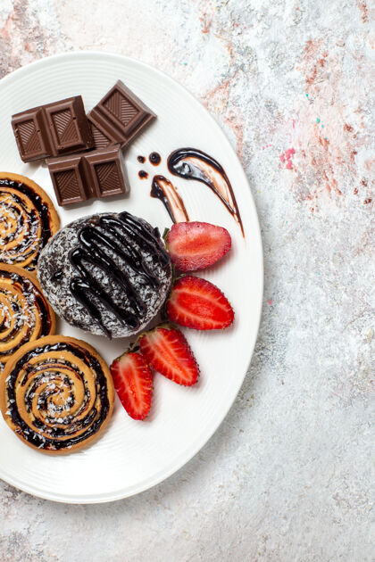 生的俯瞰美味的饼干与巧克力蛋糕和草莓上轻白色空间盘子糖饼干