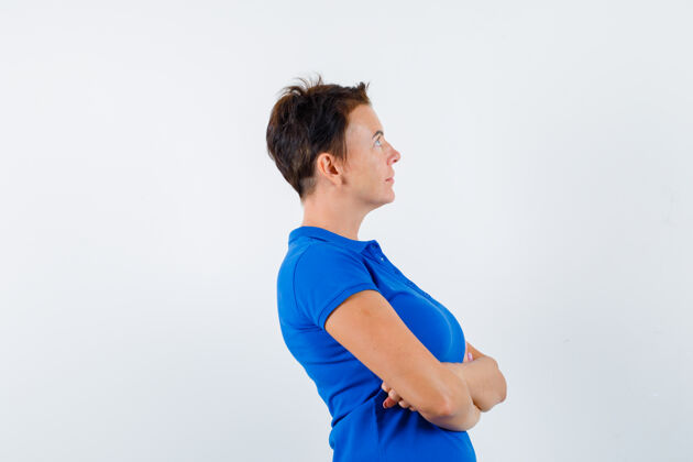 自然成熟的女人交叉着双臂站在蓝色t恤里 看起来很沉思女性交叉人