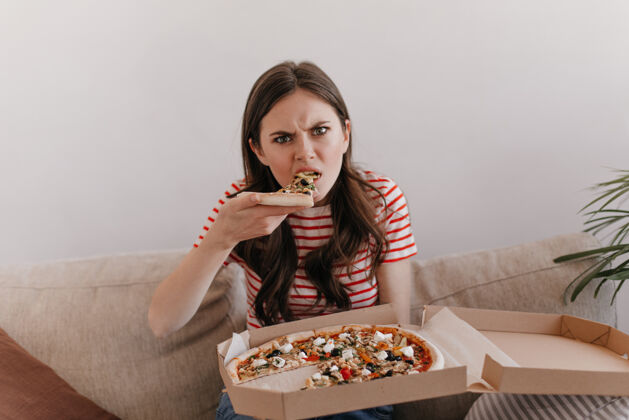 美味一个穿着条纹衬衫 饥肠辘辘的女人咬着新鲜的比萨饼肖像公寓休闲