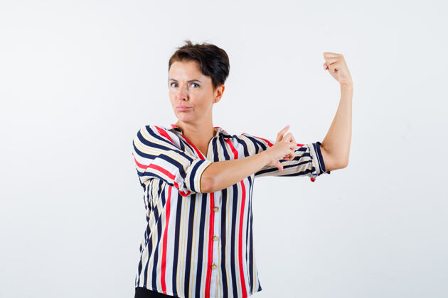 人穿条纹衬衫的成熟女性 展现力量姿态 测量肱二头肌的大小 看起来很自信 正面视图肖像显示健康