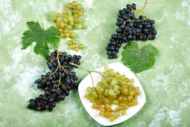 正面视图一盘白葡萄和黑葡萄的顶视图 绿色背景上有叶子高质量的照片多汁葡萄美味